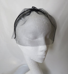 sheer black veil on a headband in tulle dress net comes to the end of the nose and covers eyes and forehead on a black metal headband easy to wear just pop on head 