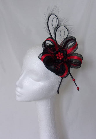 black and red cocktail fascinator hat on black and bright red on a round sinamay base with two black curl feathers at the top a bow loop in black sinamay with a stripe of red satin ribbon and a piece pf netting on red and a black satin ribbon ruffle and red pearls 