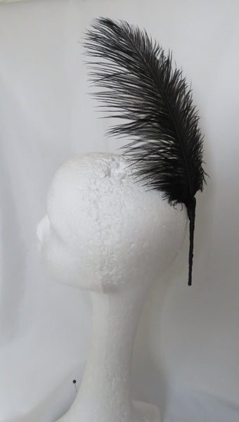 A single black feather accessory displayed on a white styrofoam mannequin head against a white fabric backdrop.