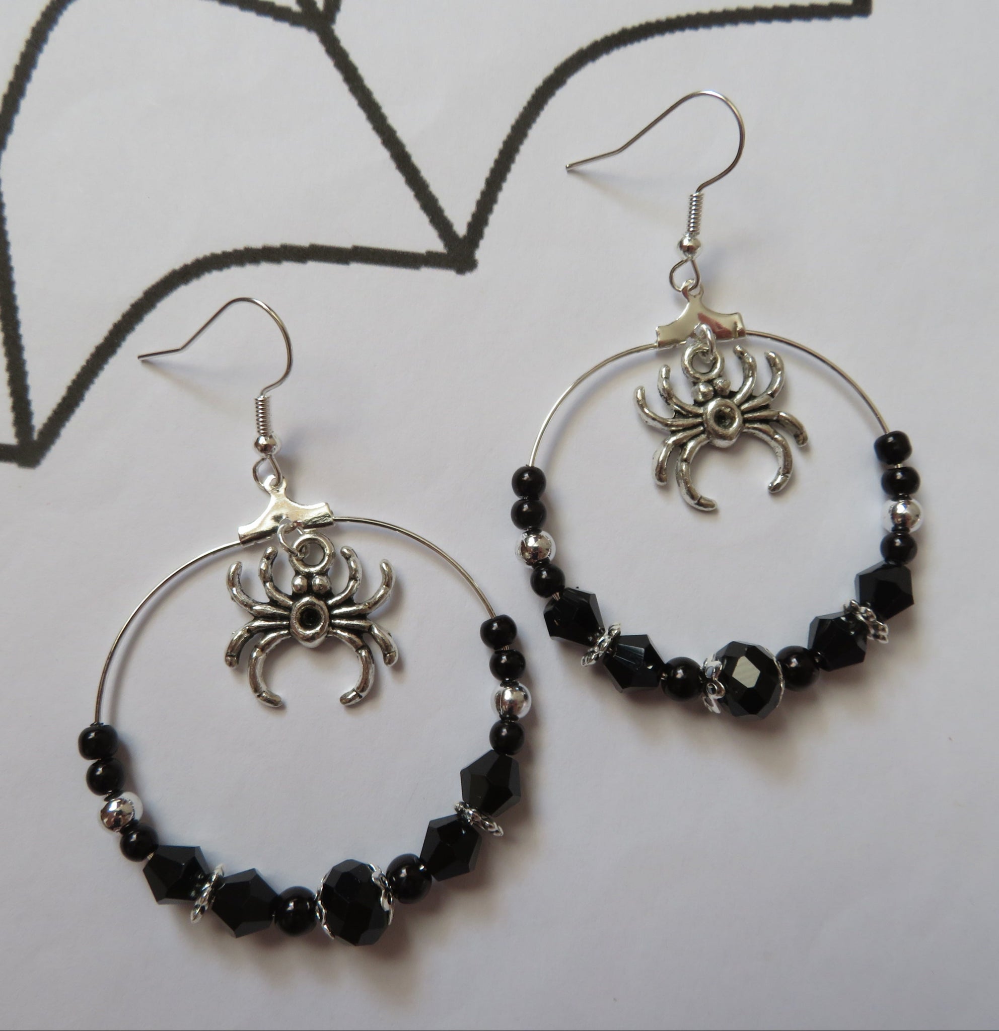 Hoop earrings with spider designs and black beads on a white background