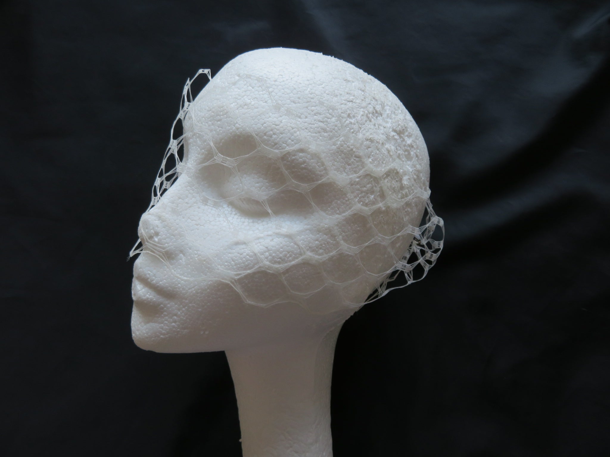 a soft ivory veil for a bride costume or party in a vintage waffle weave veiling which has large holes about the size of a 50 pence very dramatic fabric narrow so that it just covers the eyes with two black or coloured hair grips or kirbi grips on either end to fix in the hair at the side