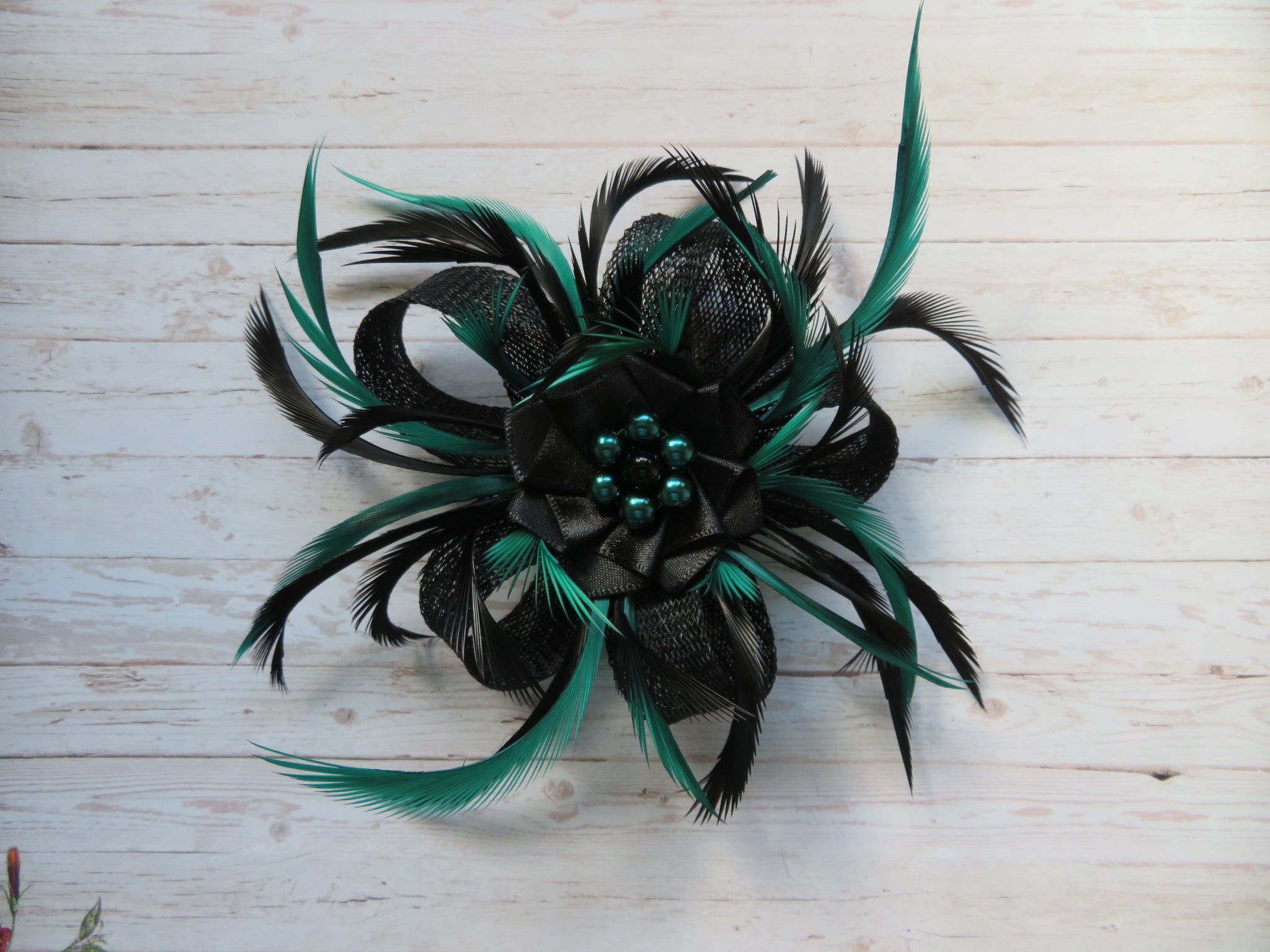 feather fascinator with long thin feathers in black and bottle green gently curling on a sinamay loop bow with a black satin ribbon ruffle with bottle green pearls in a flower shape attached to the head with either a small hairclip comb or on a headband made to order