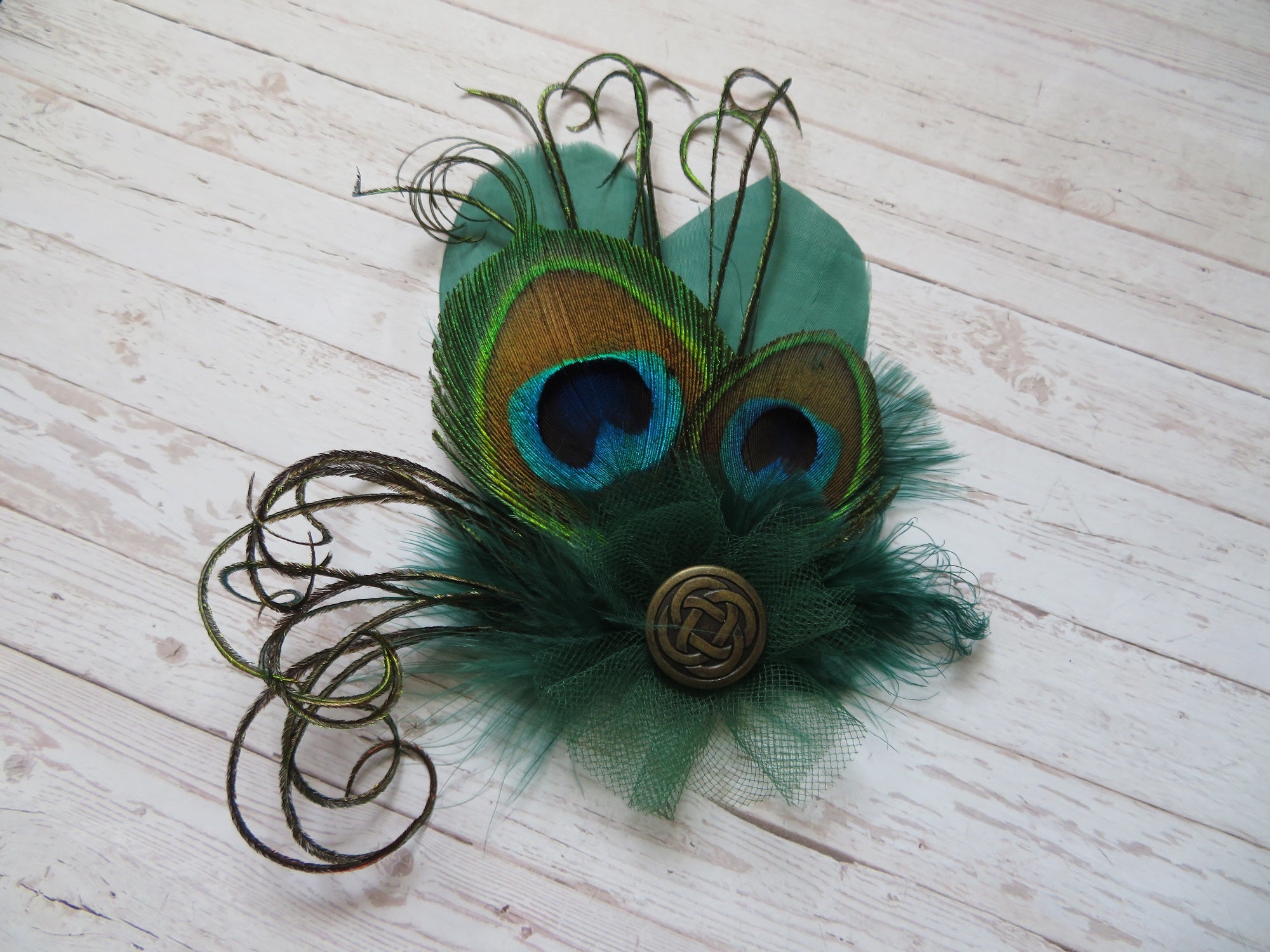 small bottle green feather hair clip with two trimmed peacock feathers curled fronds and a tulle ruffle and brass celtic button