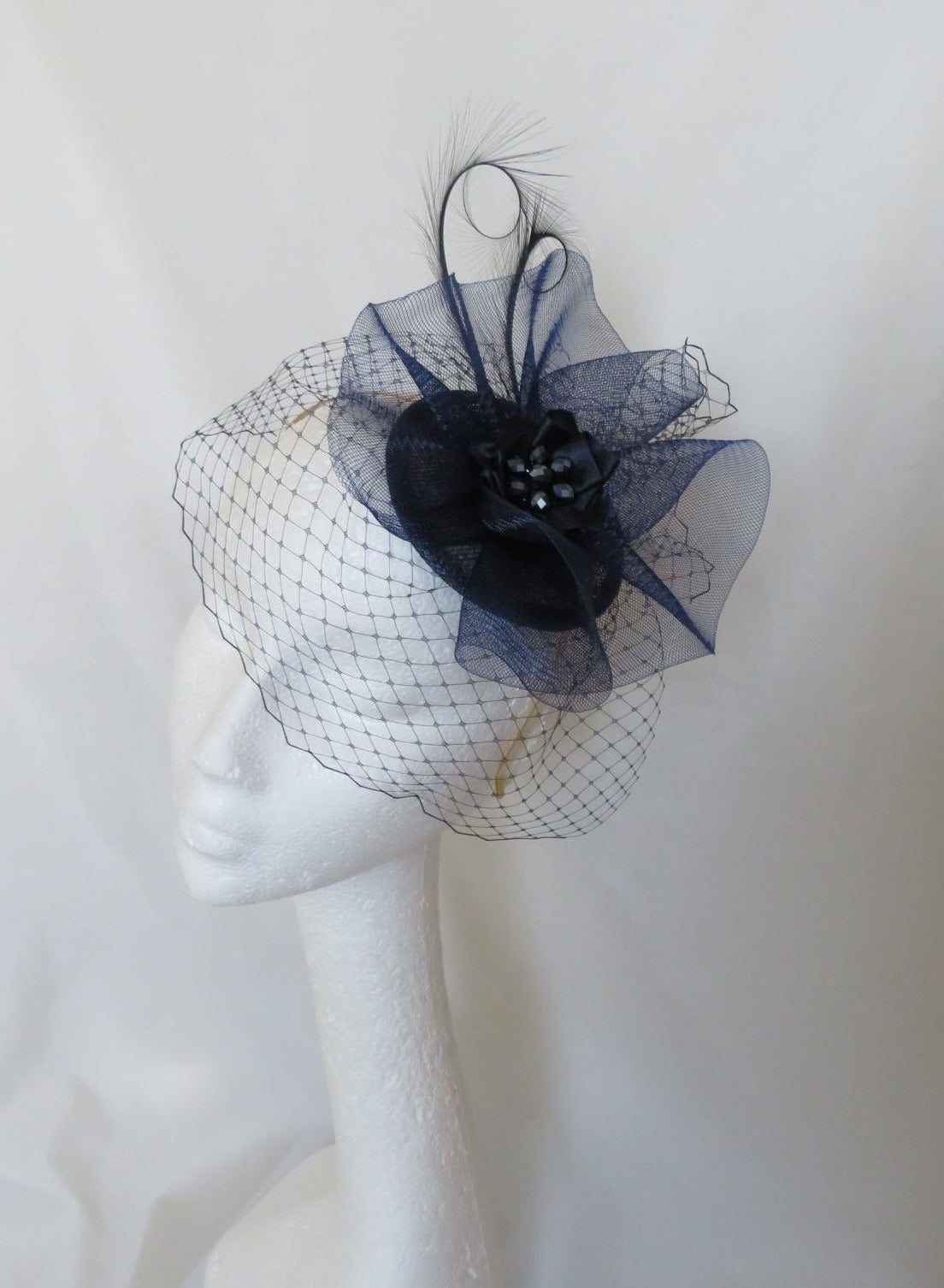 navy blue fascinator hat with a veil and a crinoline bow and curl feathers at the top finished with ribbon ruffle and crystal cluster