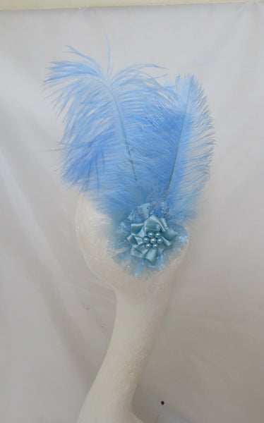 A light blue feather fascinator or hair accessory displayed on a white mannequin head, set against a white fabric backdrop.