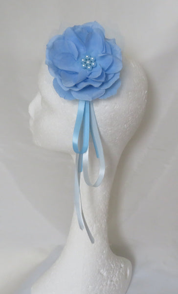 A light blue fabric flower headband with a matching ribbon tail, displayed on a white styrofoam mannequin head against a draped white fabric background.