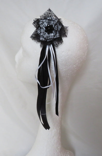 A black and white lace hair accessory with long ribbon tails, displayed on a white mannequin head against a white fabric backdrop.